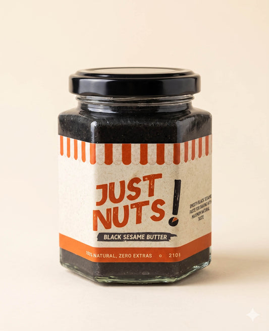 A glass jar of Just Nuts Black Sesame Butter with a black lid and a cream-colored label featuring orange text and stripes, set against a solid light beige background.